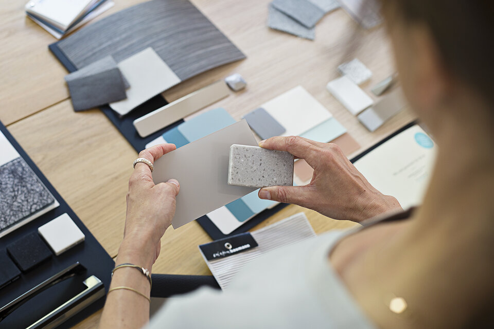 Verschiedene Materialproben liegen auf einem Tisch. Leicht von oben fällt der Blick über die Schulter der Person, die verschiedene Materialproben nebeneinander hält.